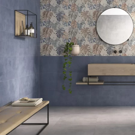 Modern bathroom interior featuring Eleganza Blu wall tiles in 333x1000mm, shown in a deep blue concrete style finish, paired with botanical patterned accent tiles, a round mirror, wooden vanity, hanging plant, and minimalist shelving.